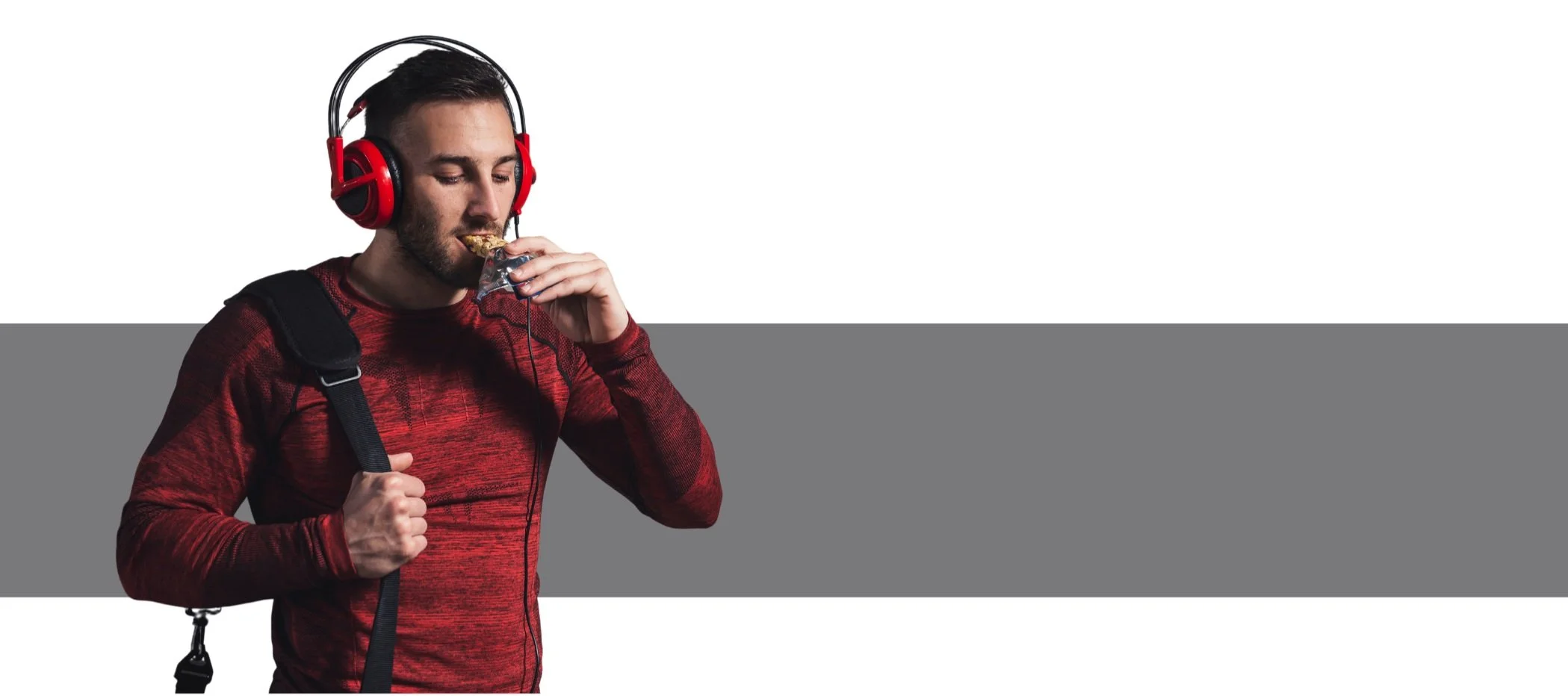 Man wearing red headphones and red sports shirt eating snack bar with backpack